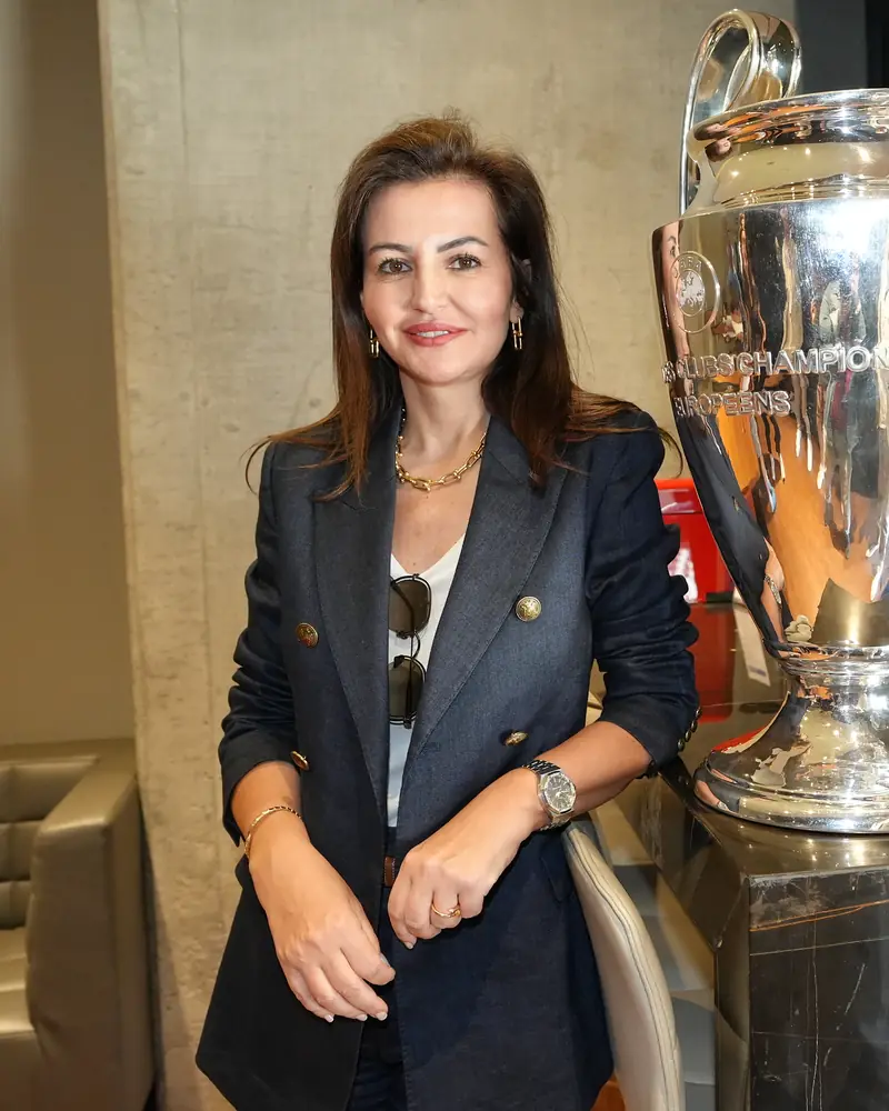 Mehtap Ferah, lacivert ceketiyle UEFA Şampiyonlar Ligi kupasının yanında.