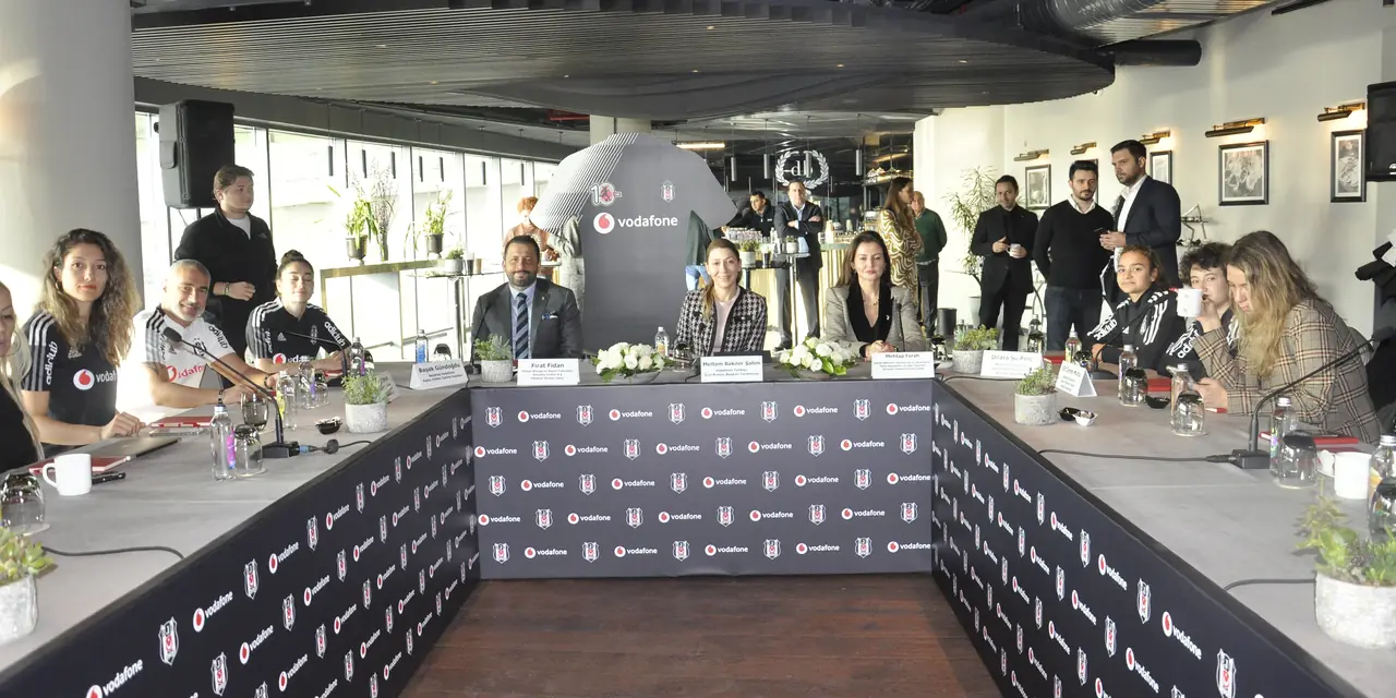 Beşiktaş logolu masaların çevresinde bir toplantı; ortada Mehtap Ferah, yanlarında Beşiktaş formalı kadın futbolcular ve diğer katılımcılar.