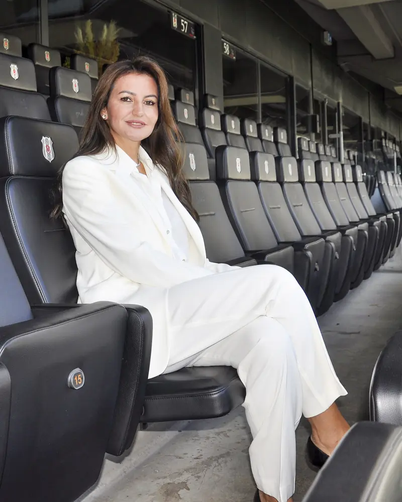 Mehtap Ferah, beyaz takım elbisesiyle Beşiktaş Stadyumu’nun locasında, siyah koltuklardan birinde oturuyor.