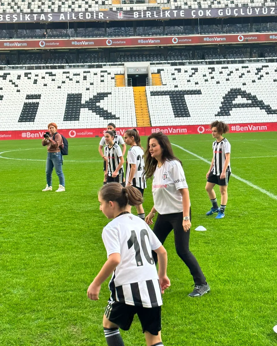 Mehtap Ferah, stadyumda formalı kız futbolcularla birlikte sahada; arka planda “Beşiktaş ailedir. Birlikte çok güçlüyüz.” yazısı.
